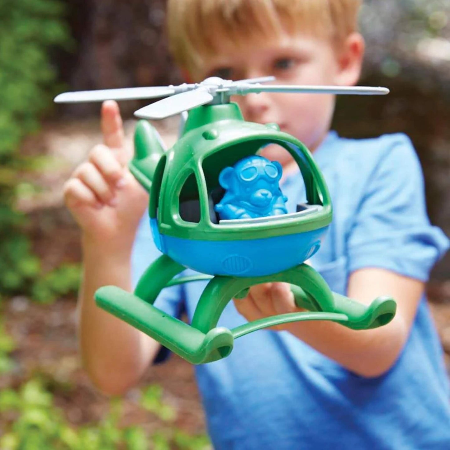 Child holding the toy helicopter mid-air, with the blue pilot visible through the front window, preparing for pretend flight.