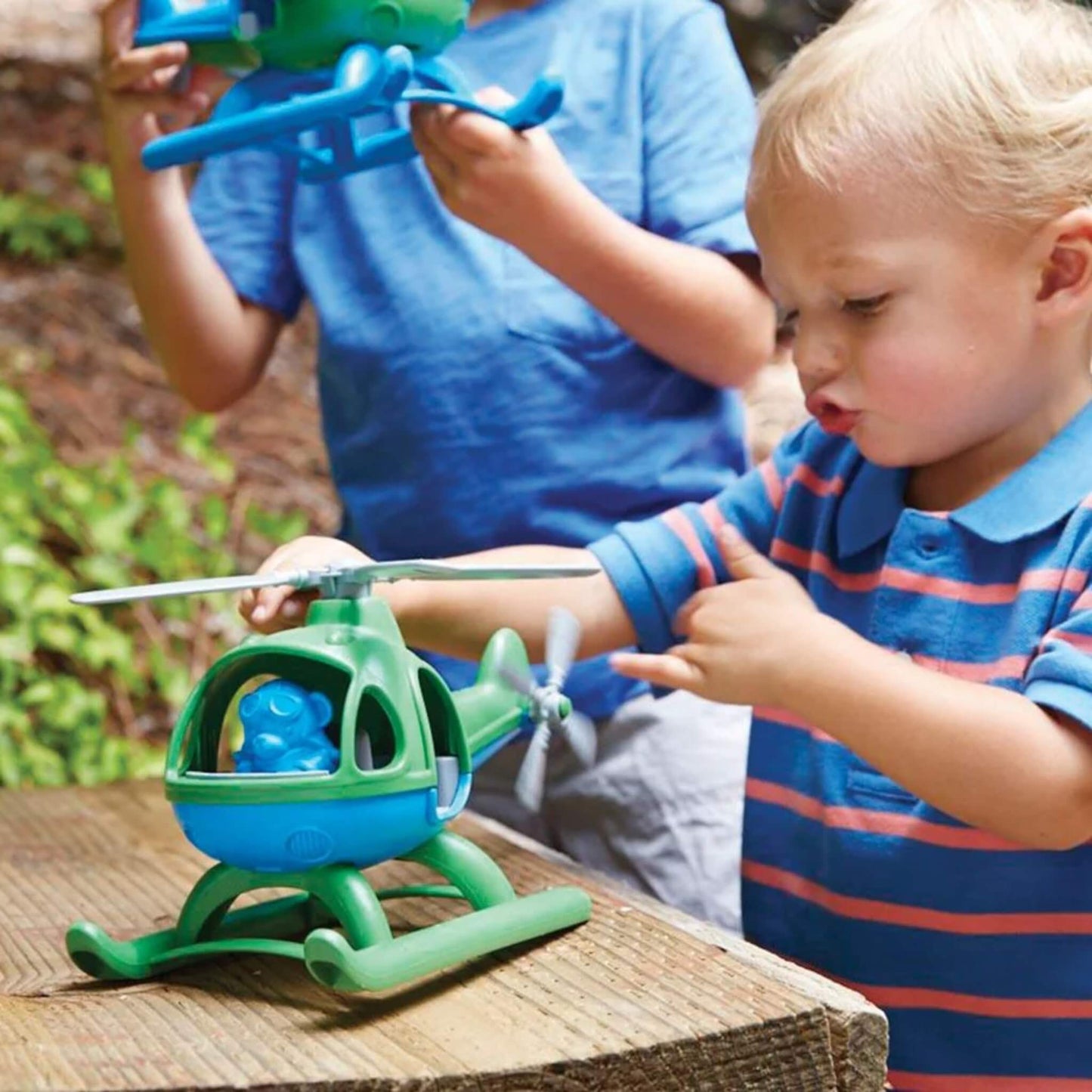 Young child pointing at the spinning rear rotor while playing with the toy helicopter on a wooden surface outside.