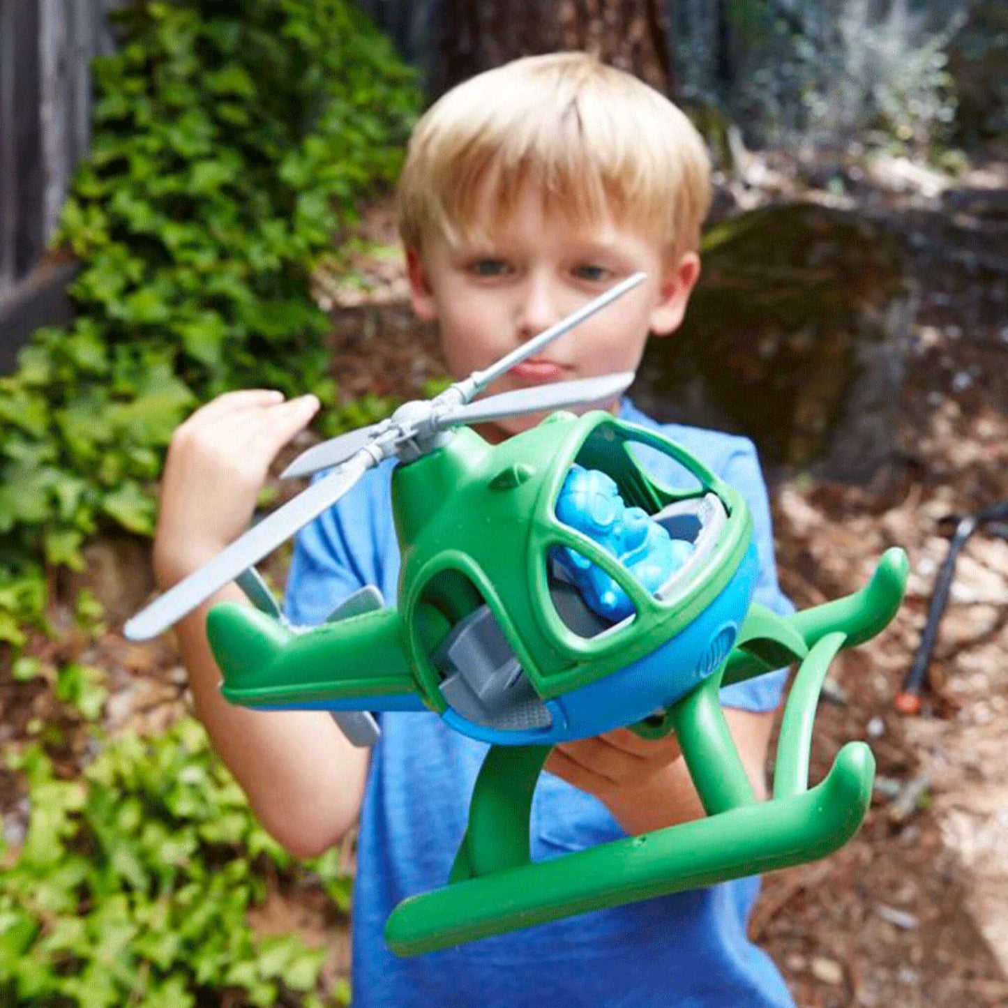 Child holding the green and blue toy helicopter out in front, showing close-up cockpit detail with the blue pilot inside.
