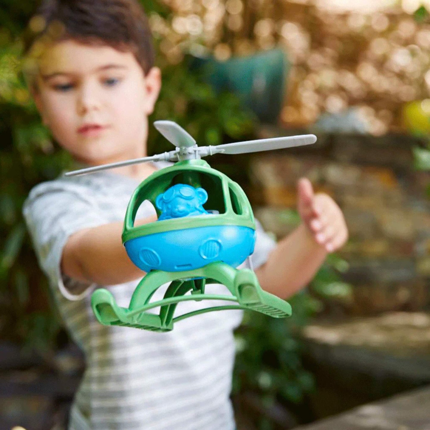 Child extending the toy helicopter forward during outdoor play, clearly showing the blue bear pilot through the cockpit window.