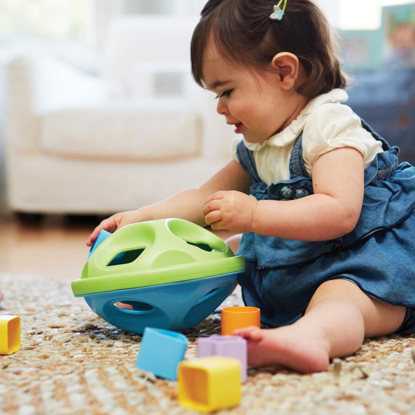 Toddler sitting on a rug, focused on posting shapes into the sorter lid placed in front of her.