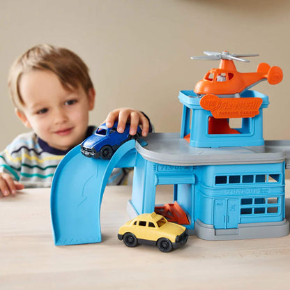 Close-up of a child using the blue ramp on the toy garage to roll down the blue car, with the yellow car parked below.