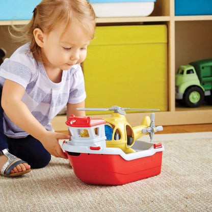 A toddler gently pushes the Green Toys Rescue Boat & Helicopter across a rug, showing its size and suitability for floor play.