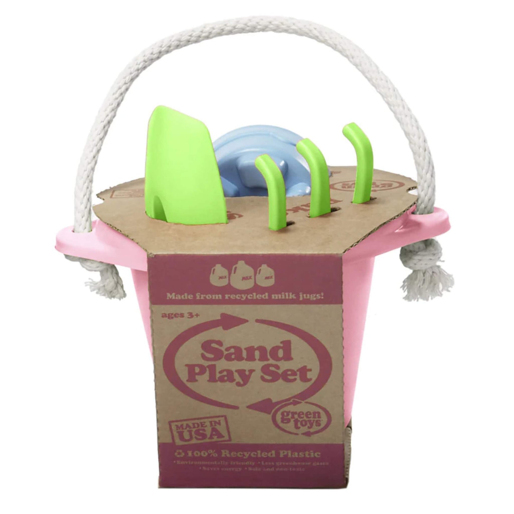 Green Toys Sand Play Set in pink shown in its cardboard packaging, with the green spade, green rake, and blue mould visible at the top. The label highlights it's made in the USA from 100% recycled plastic.