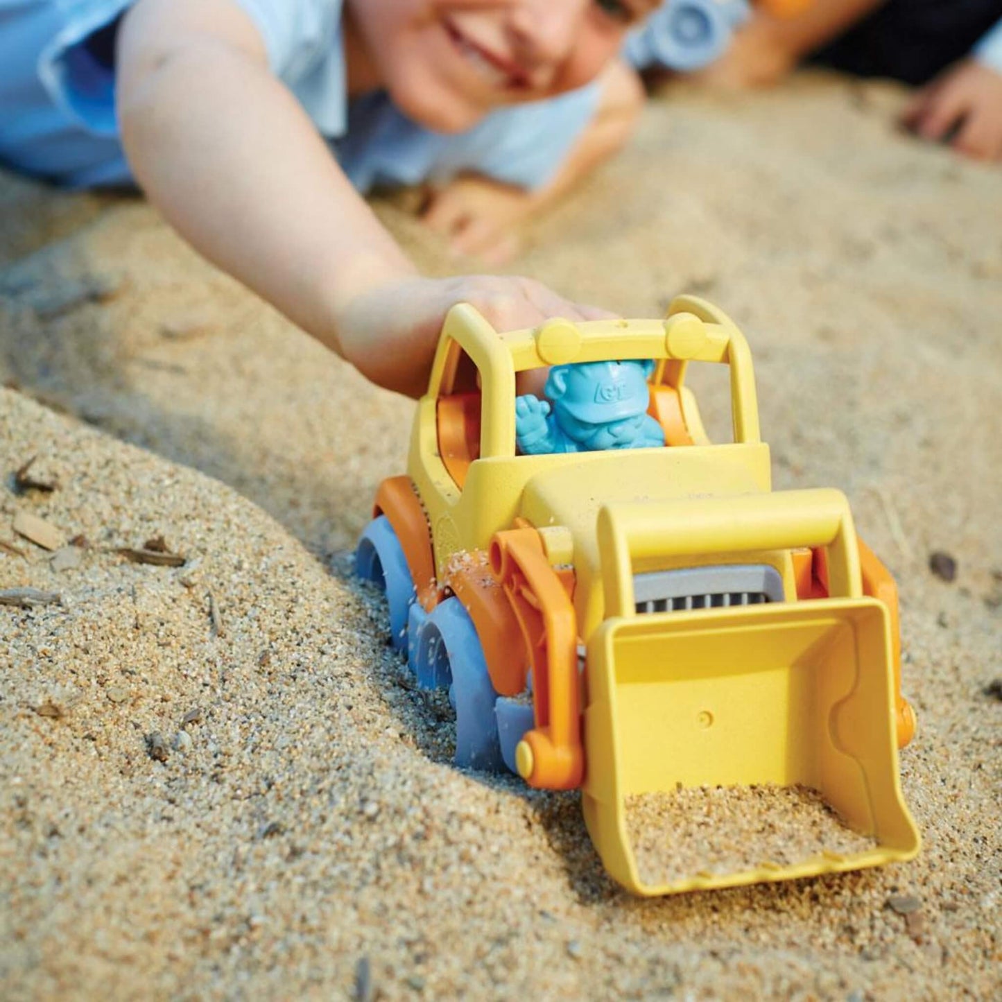 Child pushing the scooper truck through sand, with the front loader full and a blue bulldog driver figure seated in the cab.