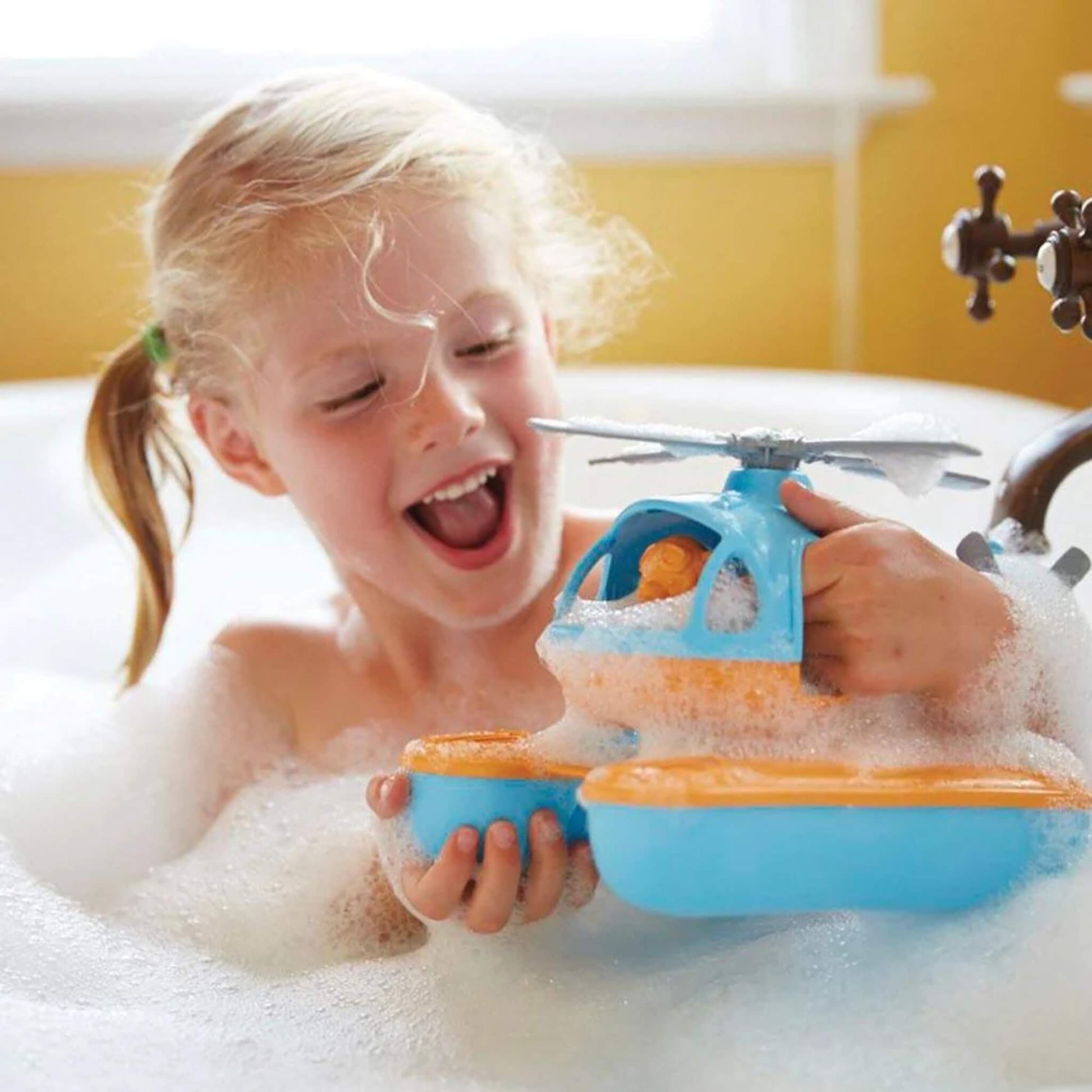 Young child in a bubbly bath, holding the Seacopter and smiling, with foam covering parts of the toy as she plays.