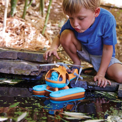 Child crouching by a garden pond, watching the Seacopter float on the surface among lily pads, with the pilot figure visible in the cockpit.