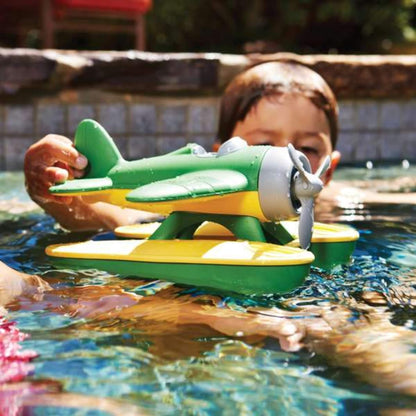 Child in a pool holding the floating Green Toys Seaplane just above the water’s surface.