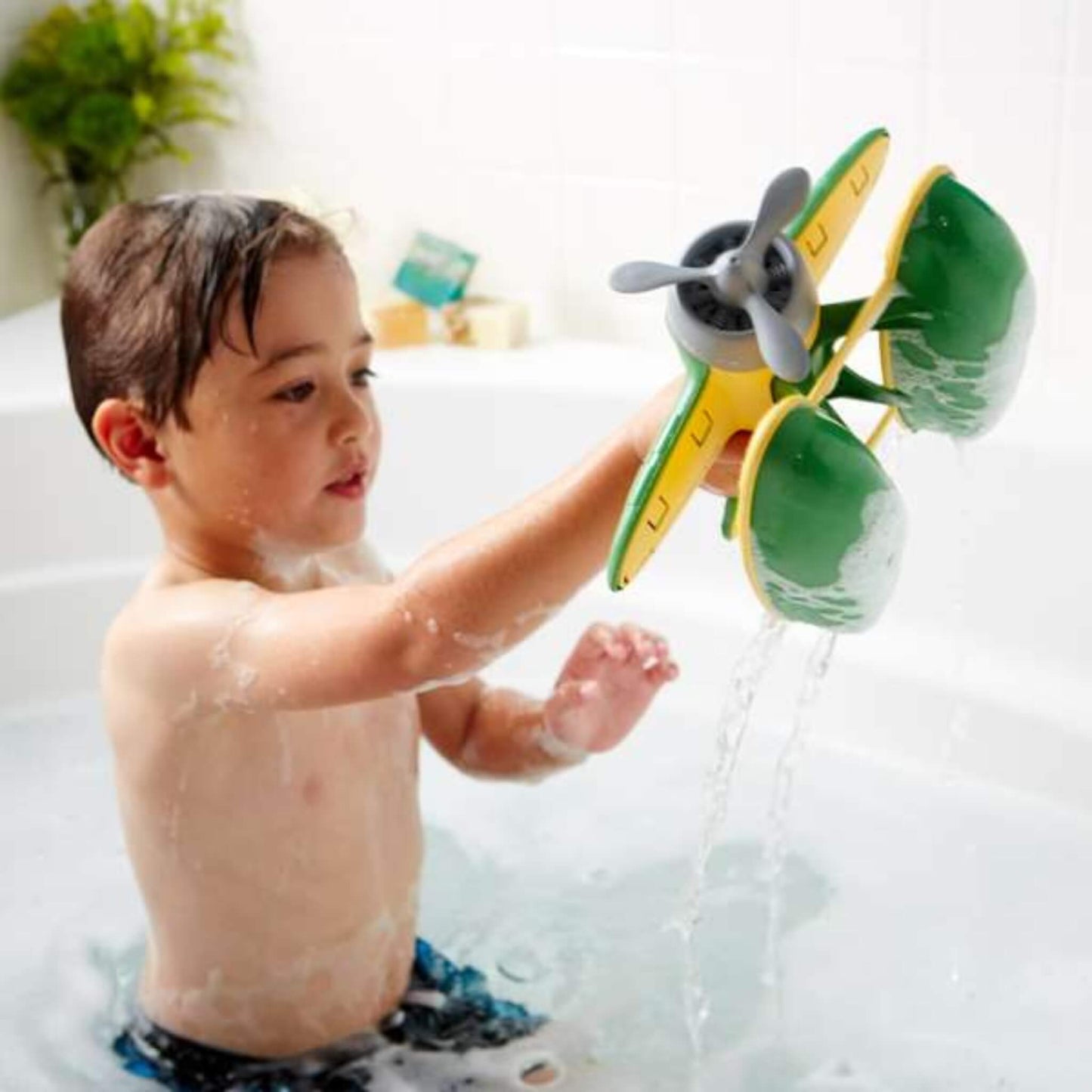 Toddler lifting the Green Toys Seaplane out of the water in the bath, with water pouring from the pontoons.