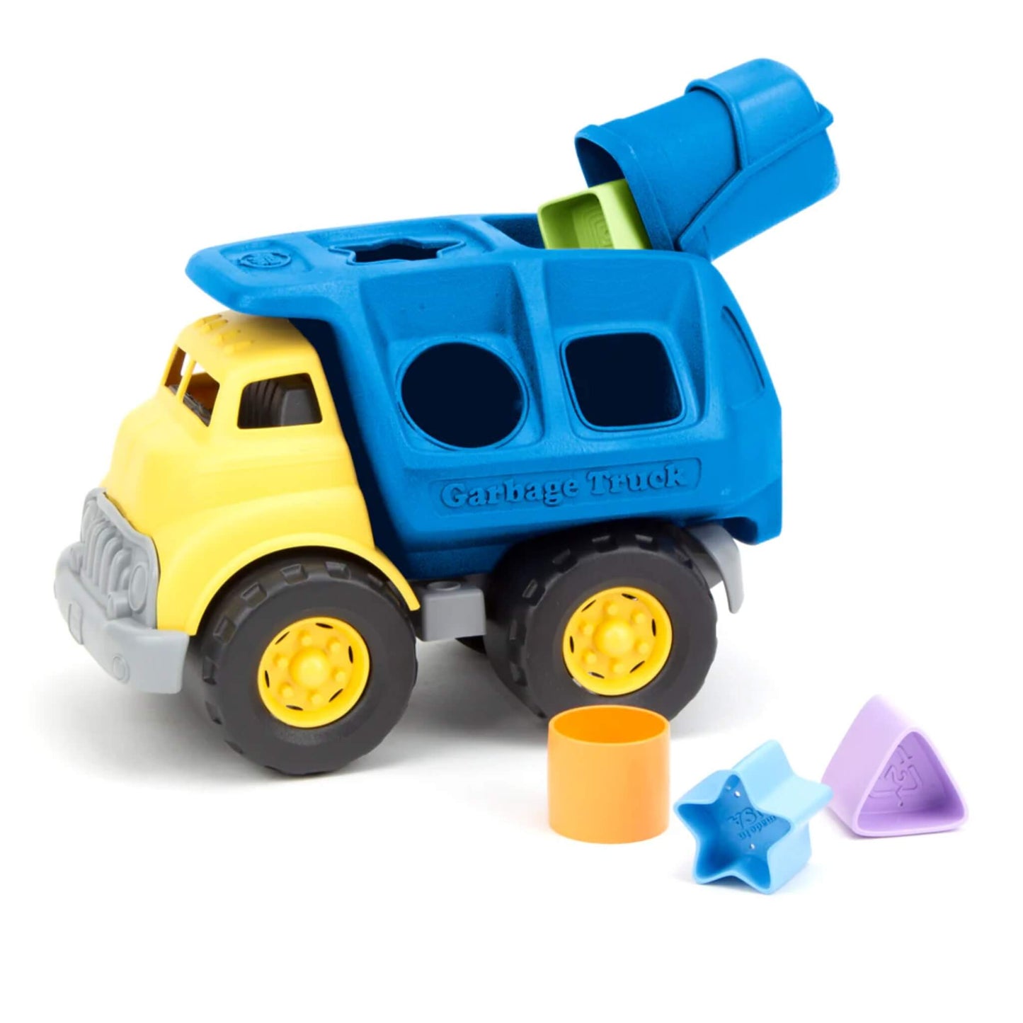 Green Toys Shape sorter truck with blue flap lifted and green square block partially dropped inside. Three shapes placed in front: circle, star, and triangle.