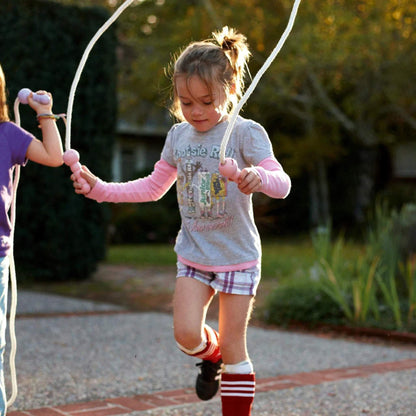 Child skipping outdoors using the Green Toys Skipping Rope with pink handles, mid-jump with both feet off the ground and rope in motion.