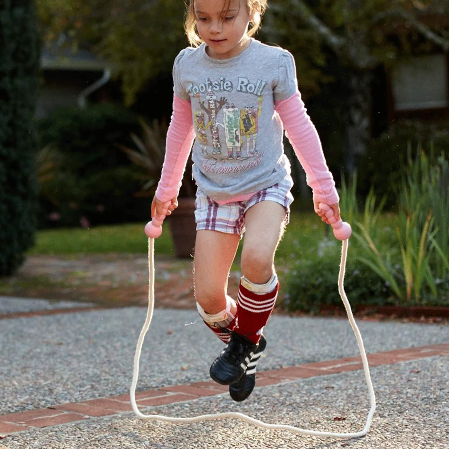 Young girl concentrating while skipping with the Green Toys Skipping Rope in pink, arms extended and rope just clearing the ground in a smooth arc.