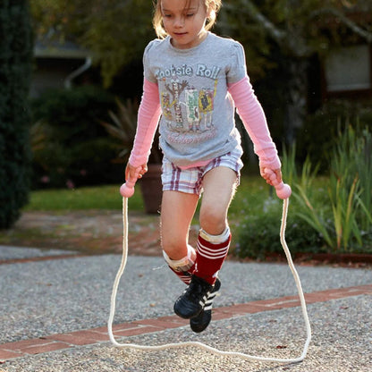 Young girl concentrating while skipping with the Green Toys Skipping Rope in pink, arms extended and rope just clearing the ground in a smooth arc.