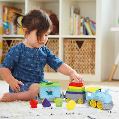 Toddler sitting on a rug placing stacking blocks onto the middle carriage of the train set, with colourful shapes scattered around.