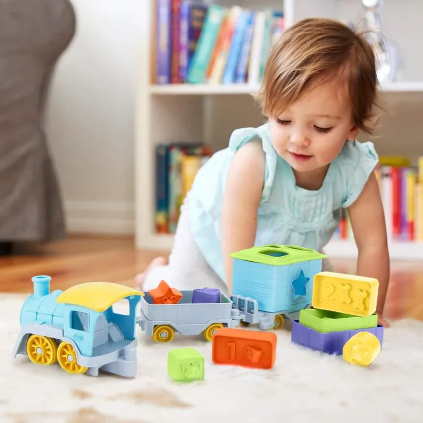 Young child playing on the floor with the train set, shapes and blocks pulled apart and arranged during open-ended play.
