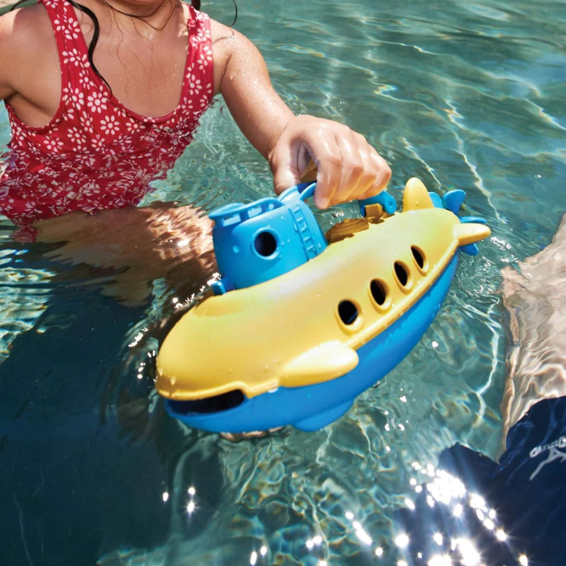 Child holding the Green Toys Submarine partially submerged in water.