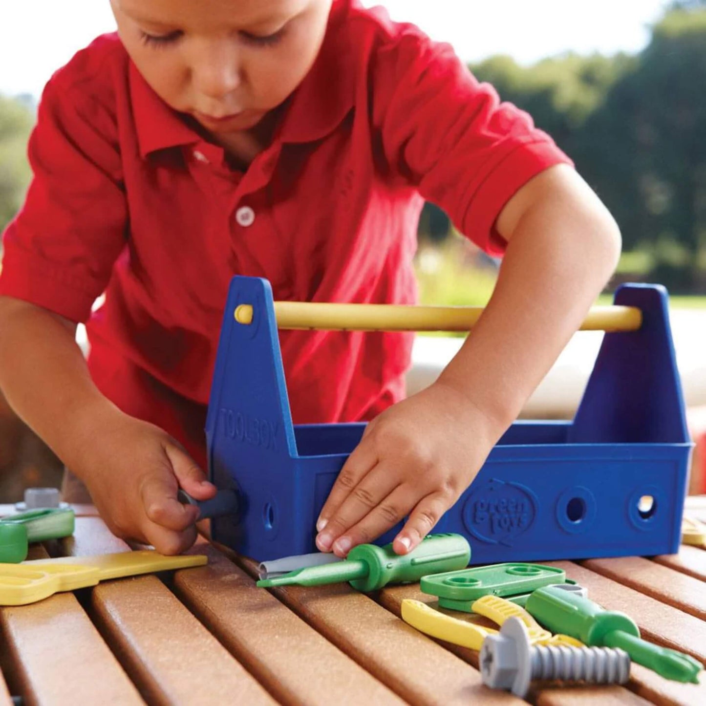 Close-up of a child using the Green Toys Tool Set, holding the toolbox steady while inserting a bolt with the green screwdriver.
