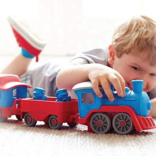 Young boy lying on the floor, smiling as he pushes the Green Toys Train along the carpet.