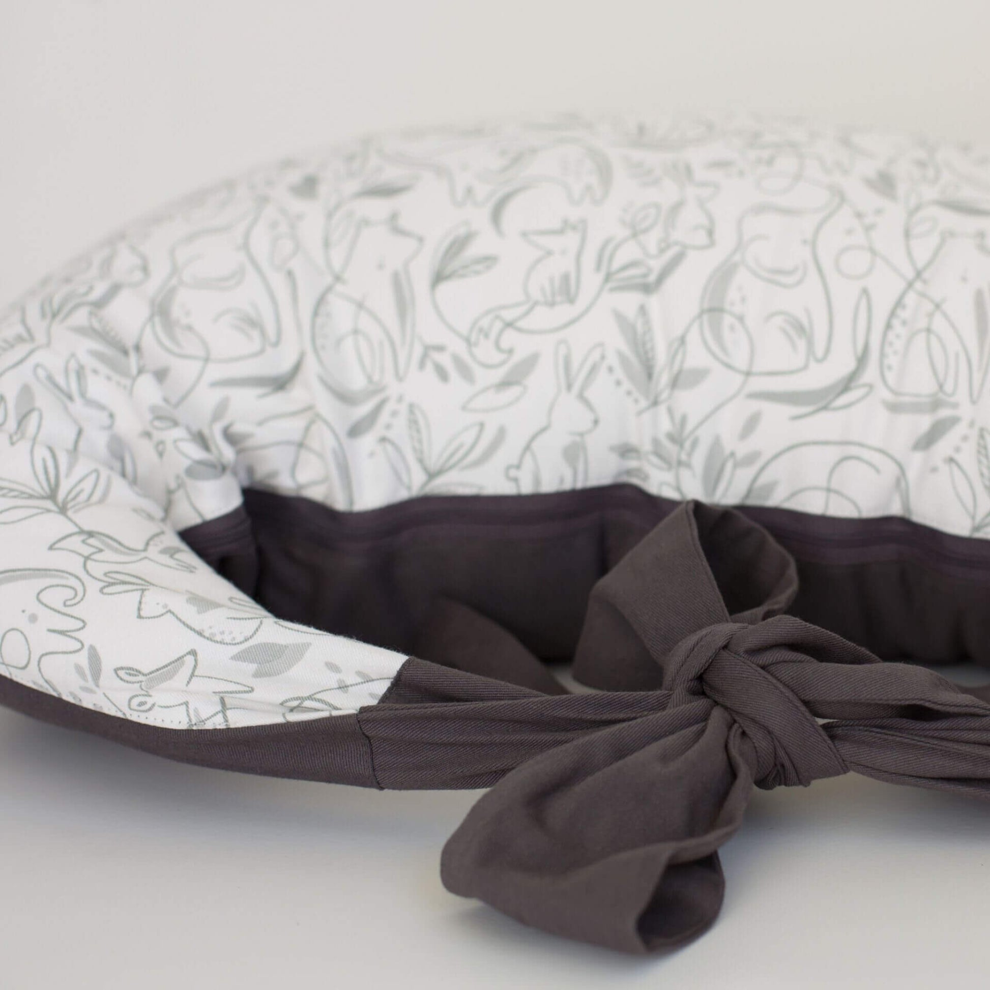 Close-up of a feeding pillow 'animal friends' fabric showing grey underside and knotted cotton ties for secure fastening.