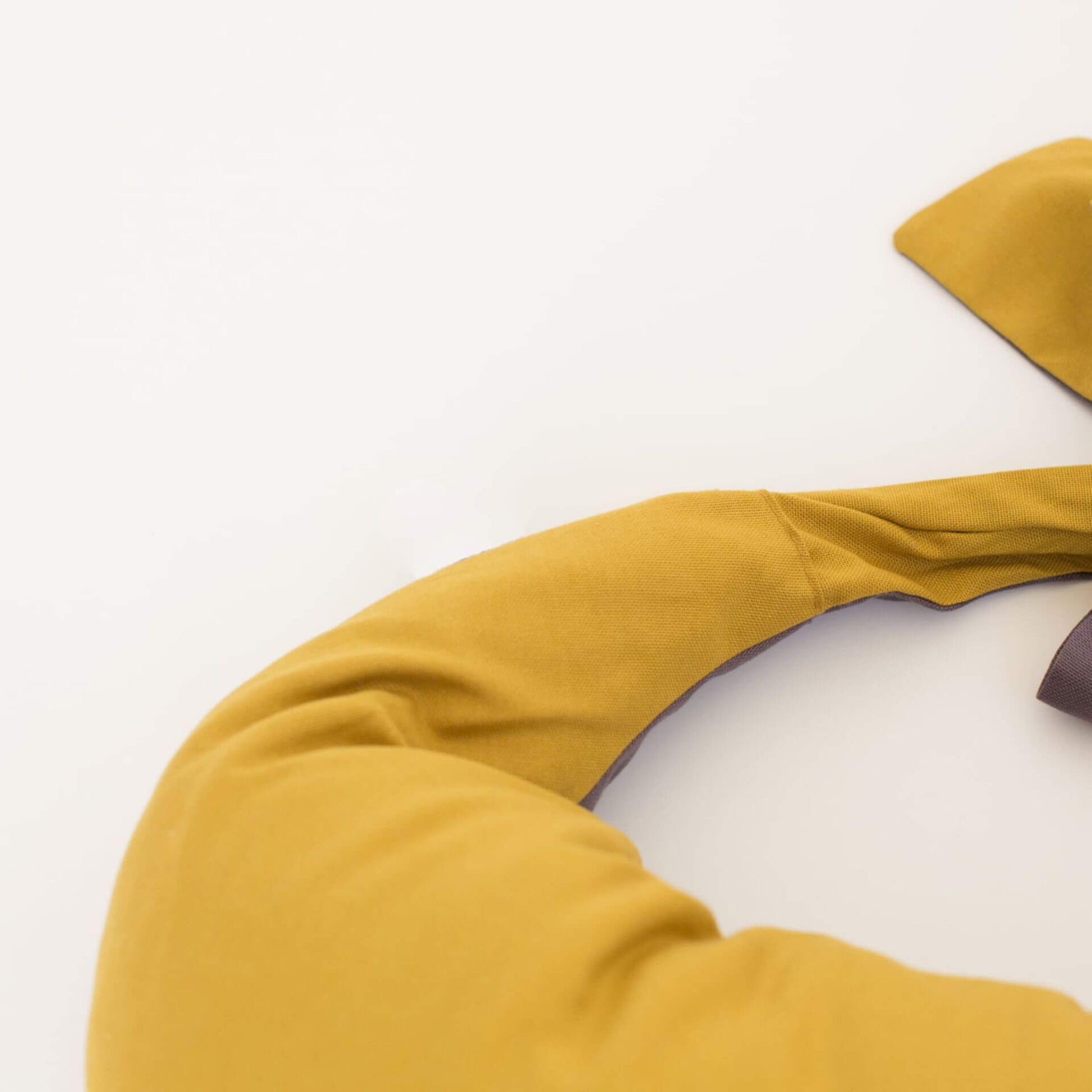 Close-up view of a crescent-shaped feeding pillow in mustard yellow with soft charcoal lining and a tied fabric fastening.