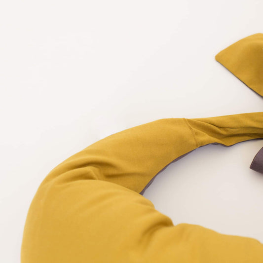 Close-up view of a crescent-shaped feeding pillow in mustard yellow with soft charcoal lining and a tied fabric fastening.