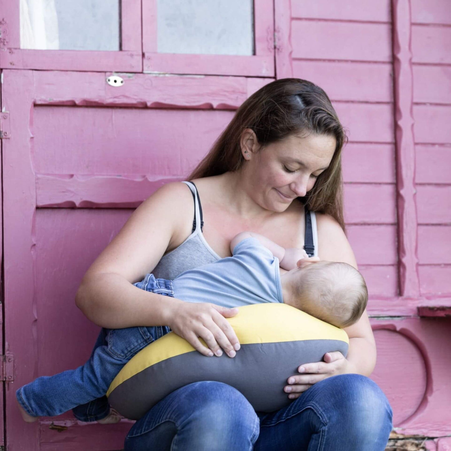 Mother breastfeeding her baby while sitting with a crescent-shaped feeding pillow across her lap for support.