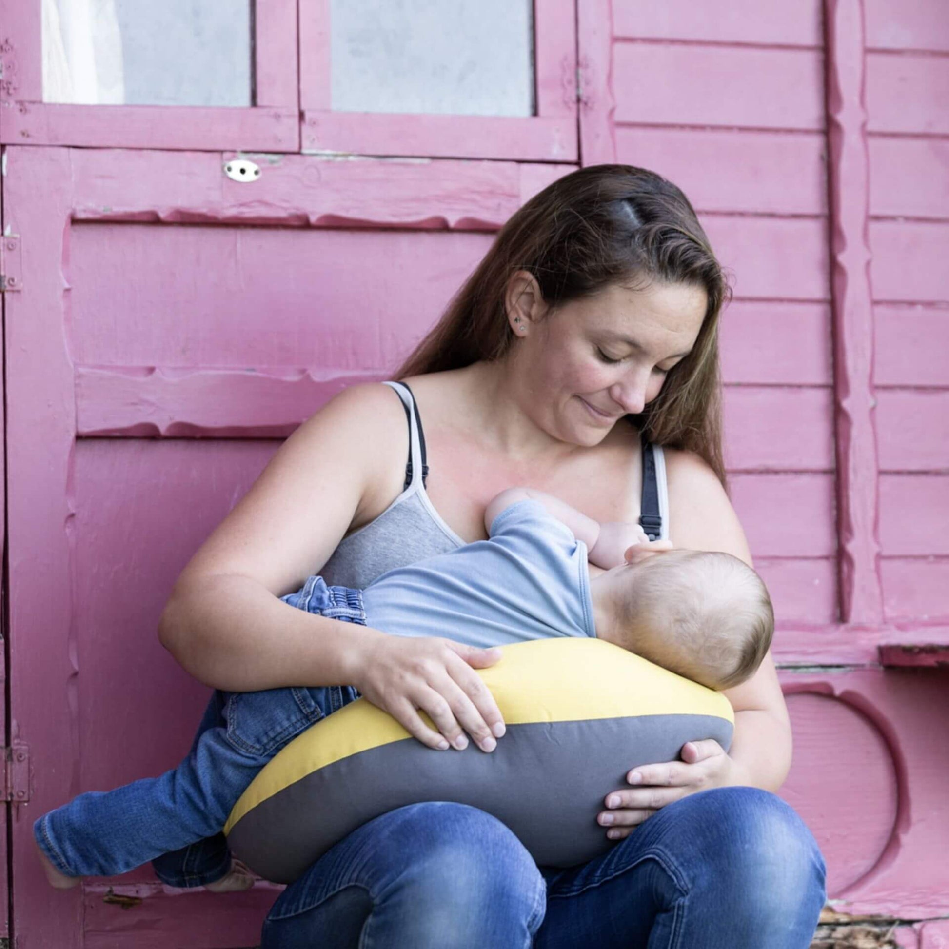 Mother breastfeeding her baby while sitting with a crescent-shaped feeding pillow across her lap for support.
