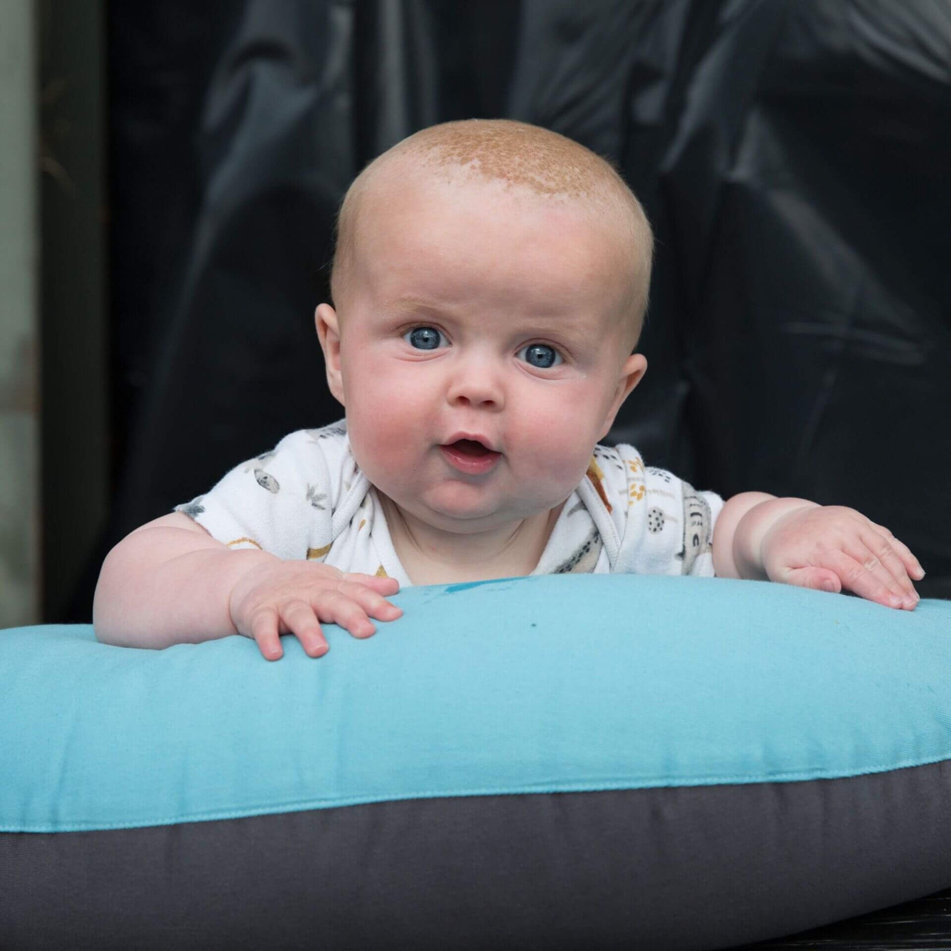Baby during tummy time resting on a supportive feeding pillow in reef blue and charcoal.
