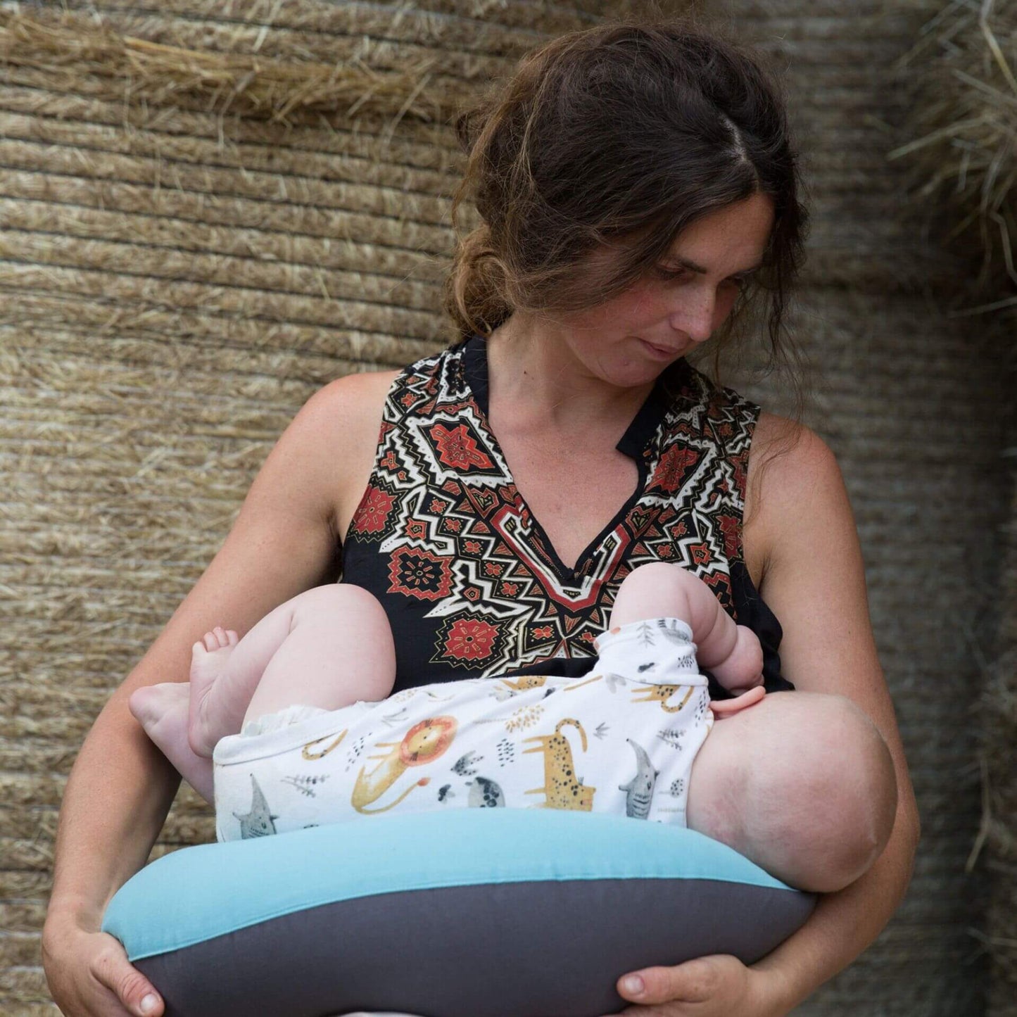 Mother breastfeeding baby using a supportive feeding pillow in reef blue and charcoal.