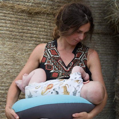 Mother breastfeeding baby using a supportive feeding pillow in reef blue and charcoal.