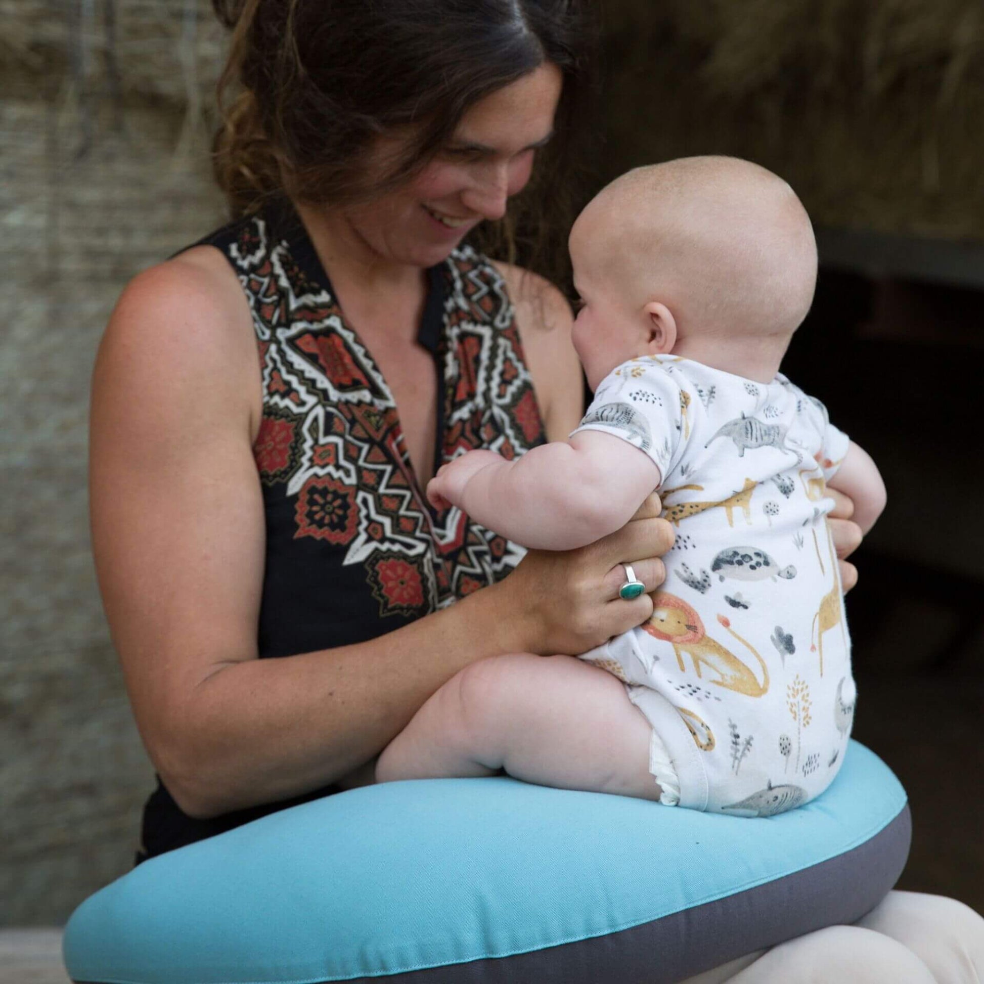 Baby sitting upright supported by a soft feeding pillow in reef blue and charcoal.