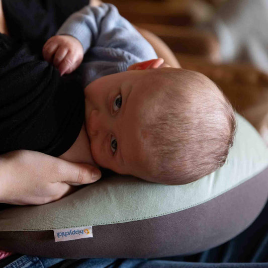 Close-up of a baby breastfeeding while resting on a crescent-shaped sage green feeding pillow with a charcoal base.