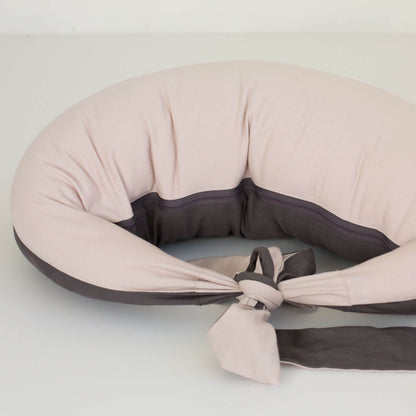 Feeding pillow in dusky pink laid flat with charcoal grey inner panel and long ties stretched out, showing its curved ergonomic design.