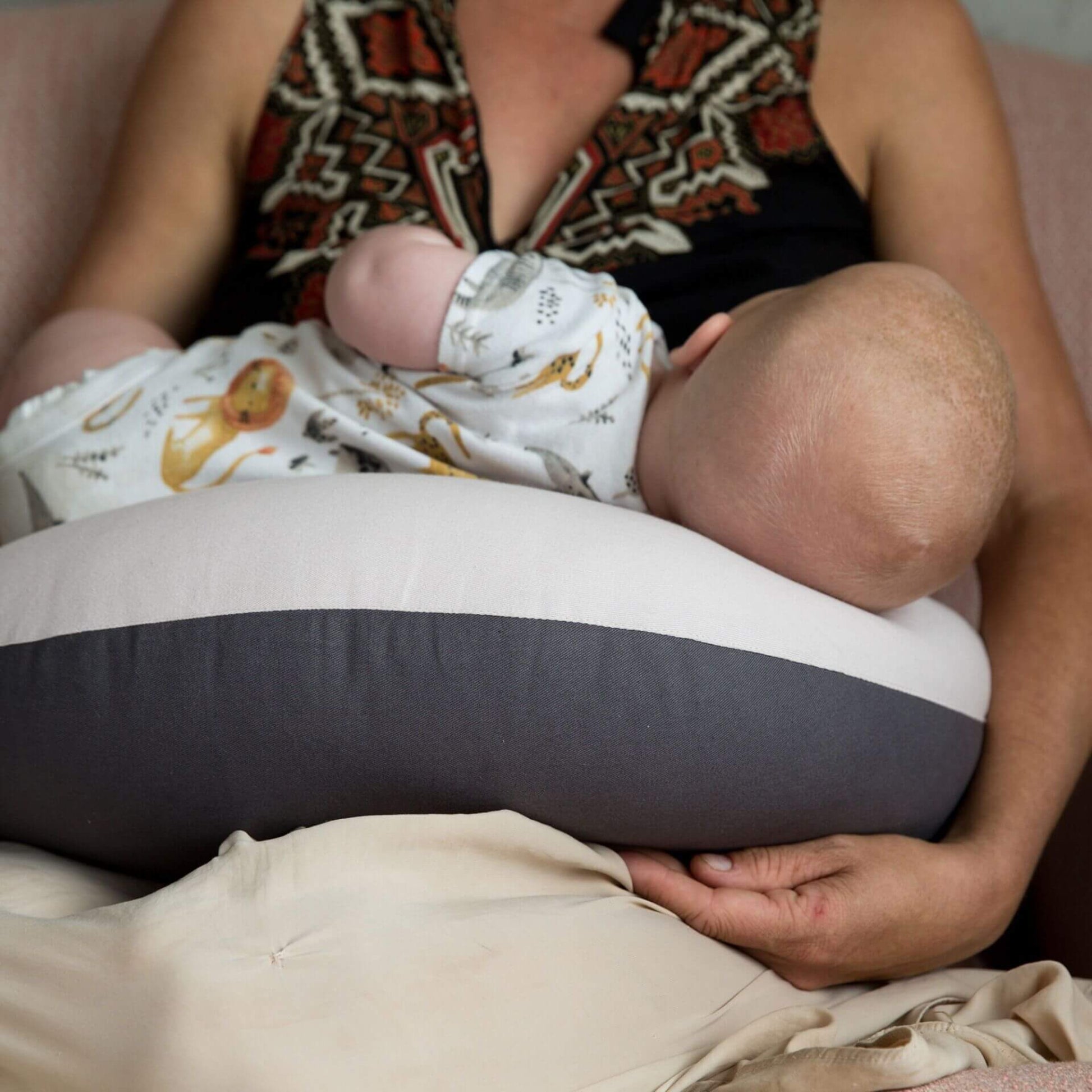 Close view of a baby breastfeeding while lying across a dusky pink feeding pillow on the mother’s lap, showing how the cushion supports baby’s body securely.