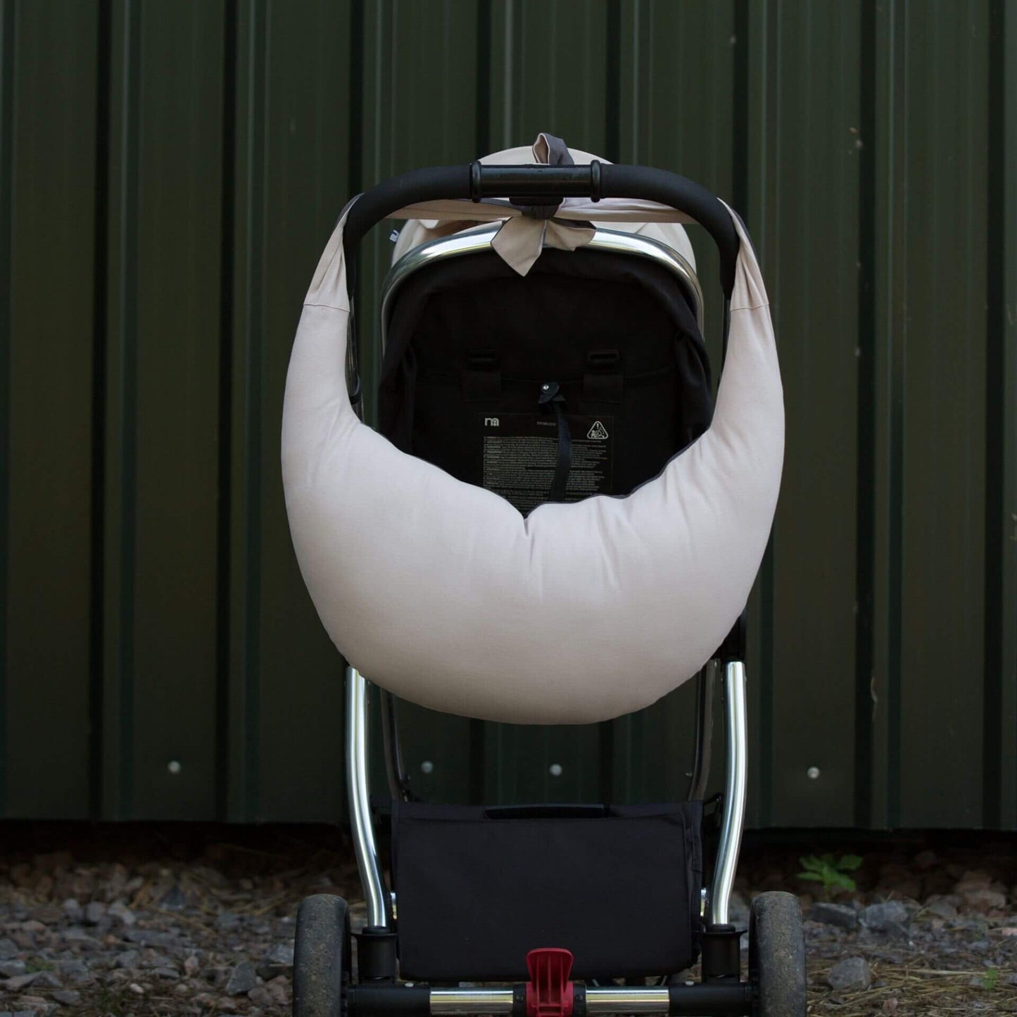 Dusky pink and charcoal feeding pillow tied to the handlebar of a pushchair, hanging neatly for transport, with its curved shape and soft fabric visible against a dark background.