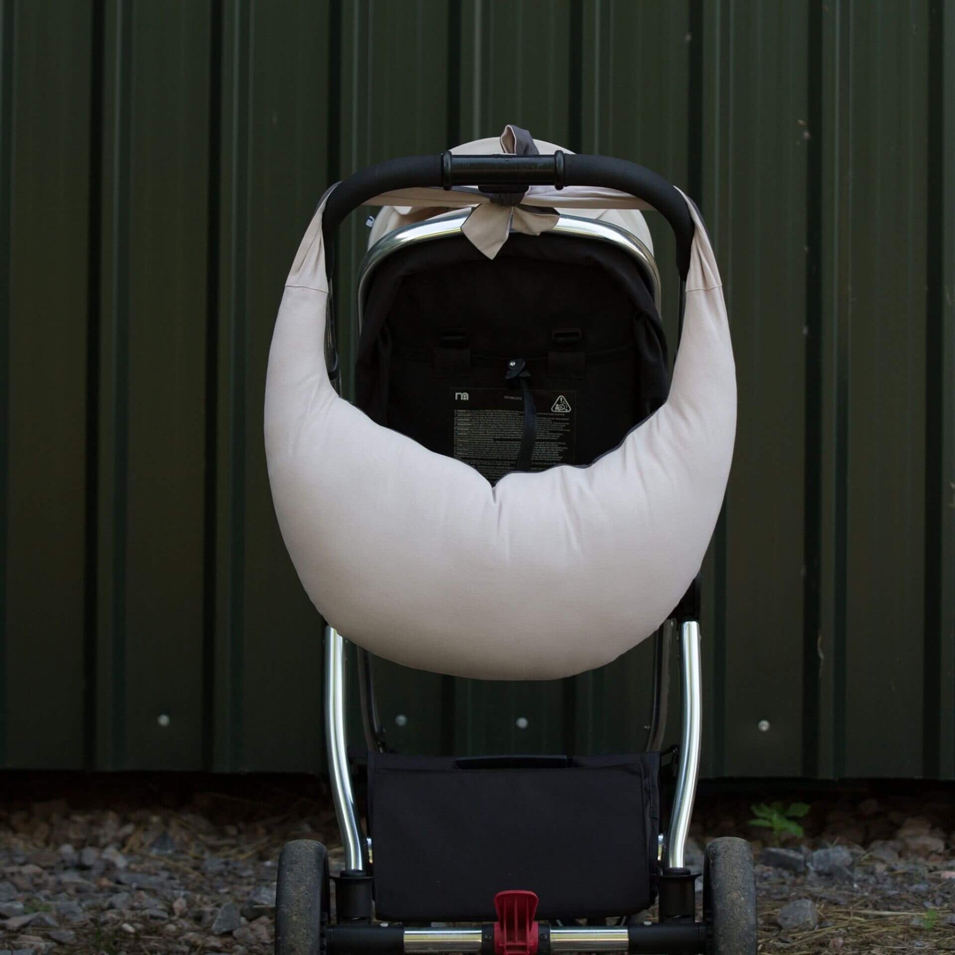 Dusky pink and charcoal feeding pillow tied to the handlebar of a pushchair, hanging neatly for transport, with its curved shape and soft fabric visible against a dark background.