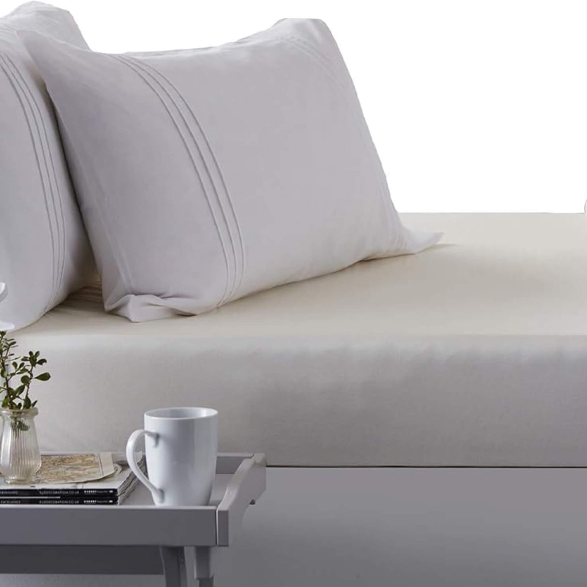 Close-up of a bed made with the Hippychick Fitted Tencel Mattress Protector, styled like a regular fitted sheet, with white pillows and a bedside tray.