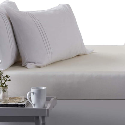 Close-up of a bed made with the Hippychick Fitted Tencel Mattress Protector, styled like a regular fitted sheet, with white pillows and a bedside tray.