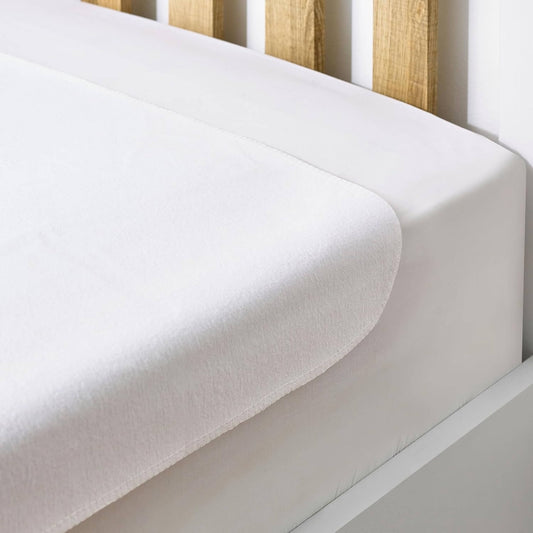 Hippychick Flat Cotton Mattress Protector neatly placed over a cot mattress with a smooth, white cotton surface.