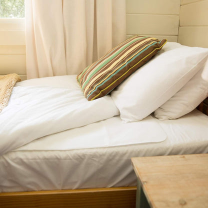 Flat tencel mattress protector laid neatly on a made bed with striped cushion and natural light from the window.