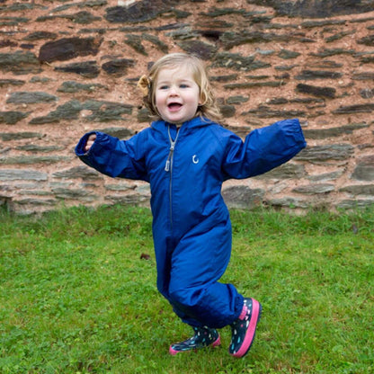 Young child playing outside in a blue waterproof suit standing near a stone wall.