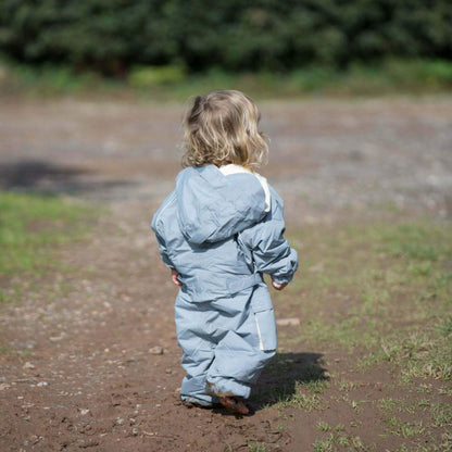 Back view of toddler walking along a muddy path wearing a grey fleece lined waterproof suit with hood up in natural light.