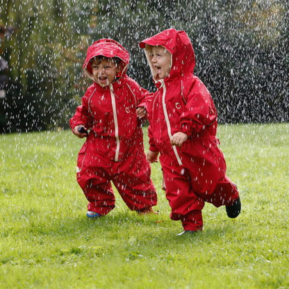Two children wearing waterproof fleece-lined suits, joyfully running together in the rain on a grassy lawn.