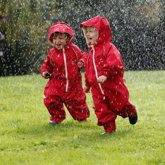Two children wearing waterproof fleece-lined suits, joyfully running together in the rain on a grassy lawn.
