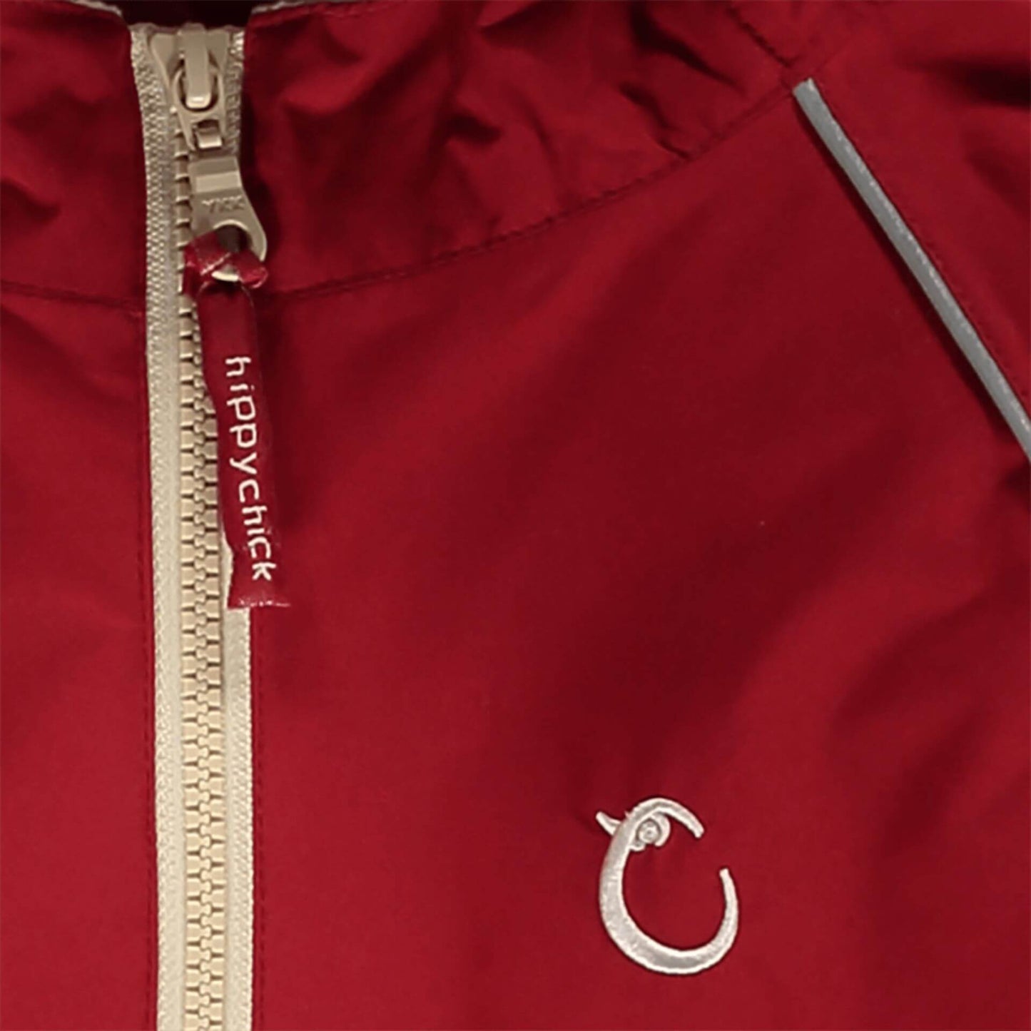 Close-up of red waterproof fabric with beige zip, showing reflective piping and embroidered Hippychick brand logo.