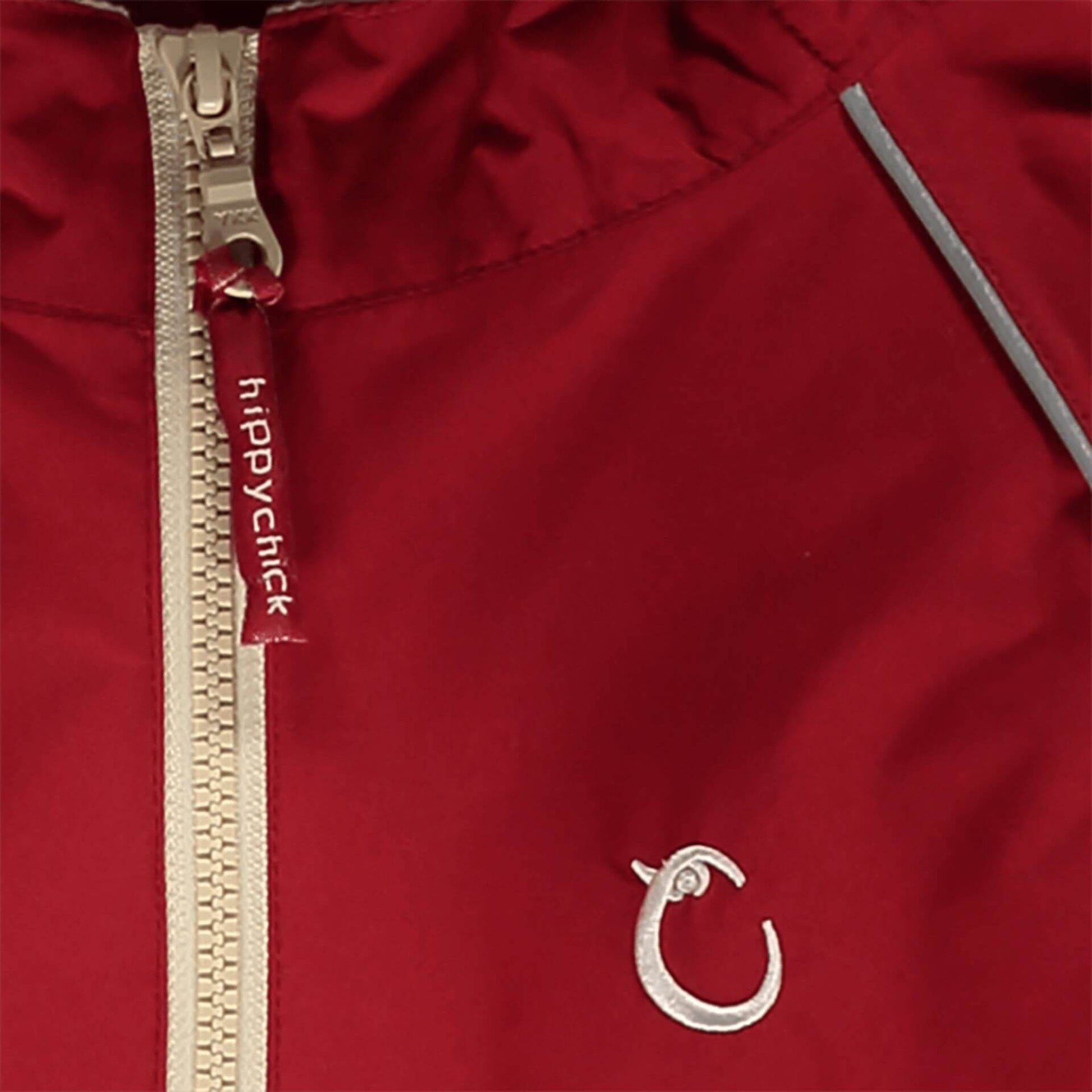 Close-up of red waterproof fabric with beige zip, showing reflective piping and embroidered Hippychick brand logo.
