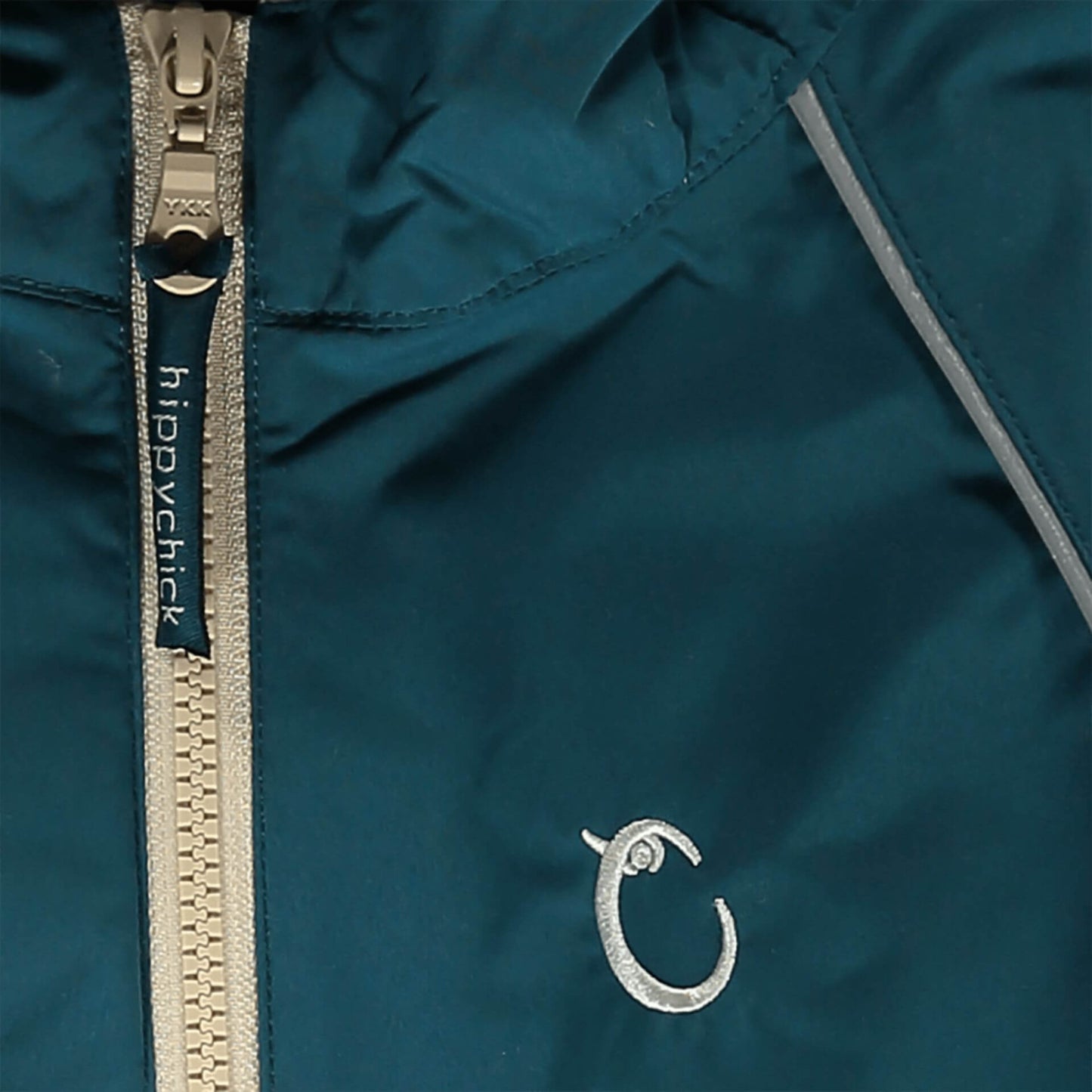 Close-up of teal waterproof fabric with beige zip, showing reflective piping and embroidered Hippychick brand logo detail.