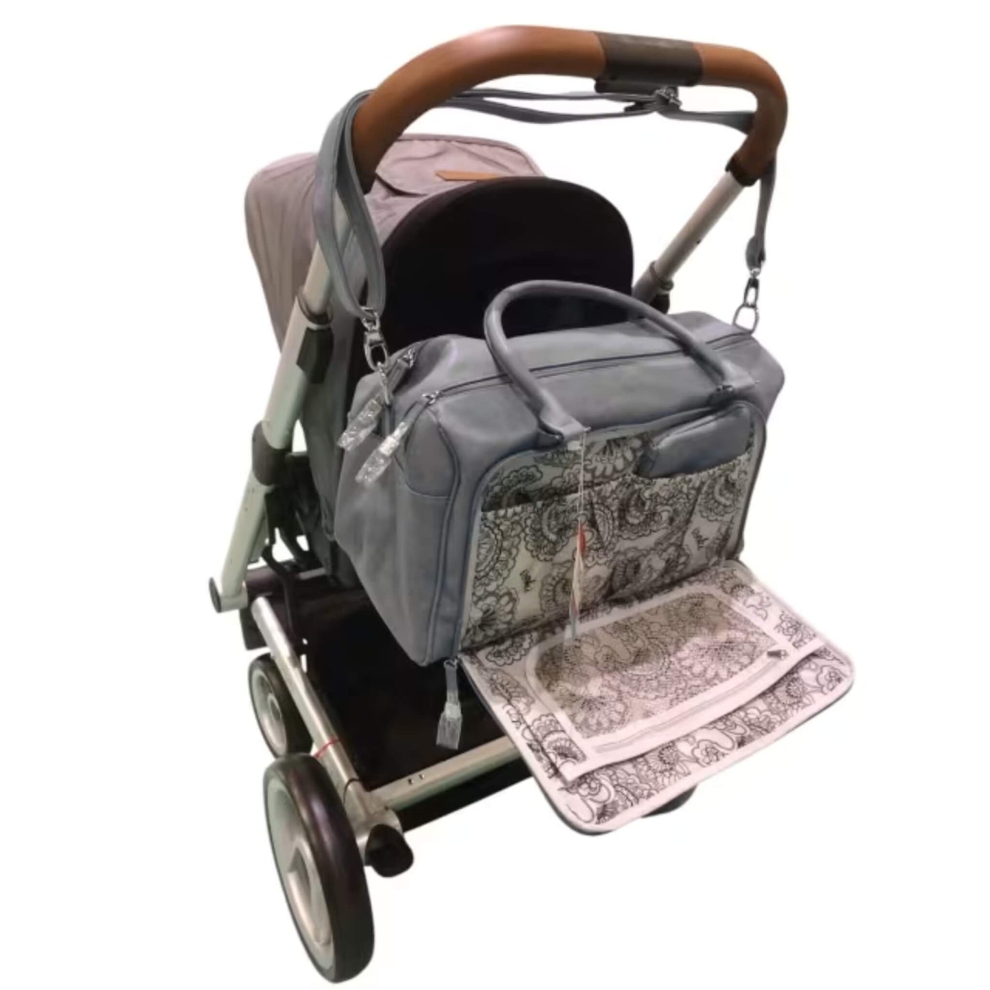 Grey changing bag attached to a pushchair handle with patterned changing mat unfolded for easy access during nappy changes.