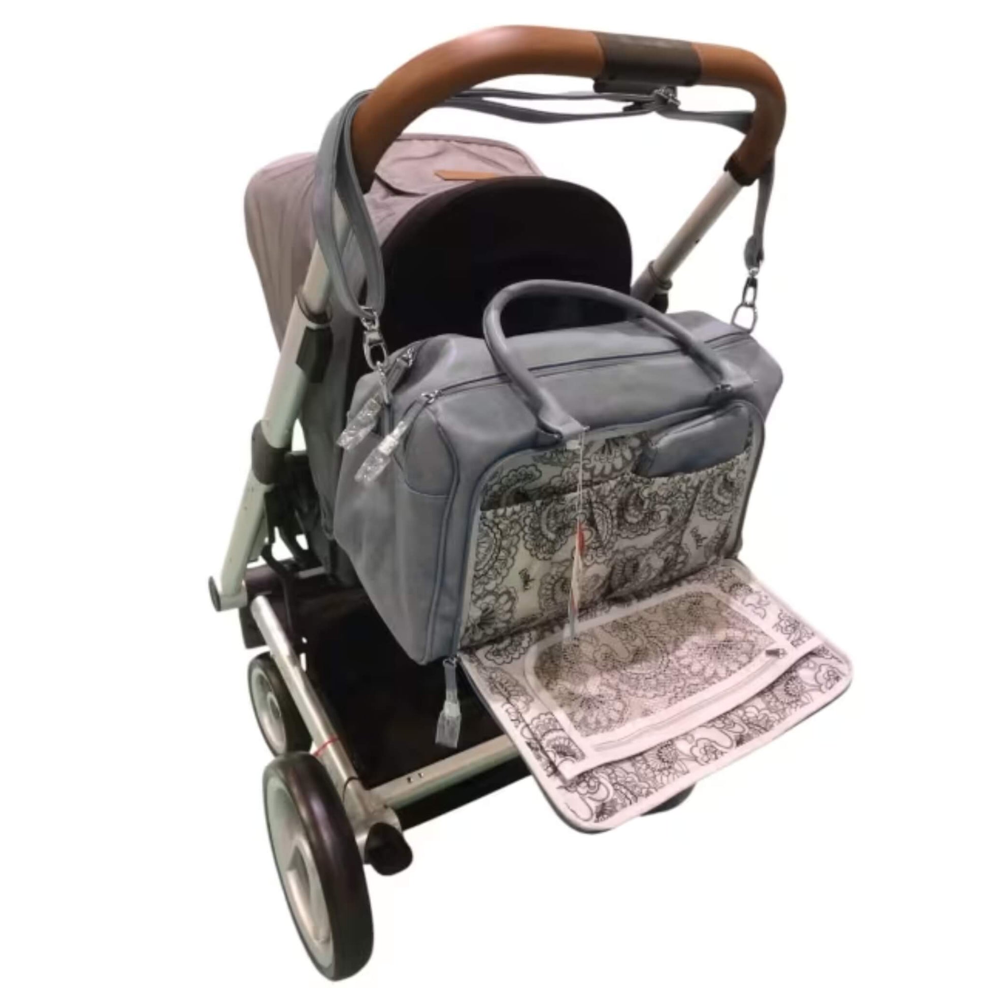 Grey changing bag attached to a pushchair handle with patterned changing mat unfolded for easy access during nappy changes.