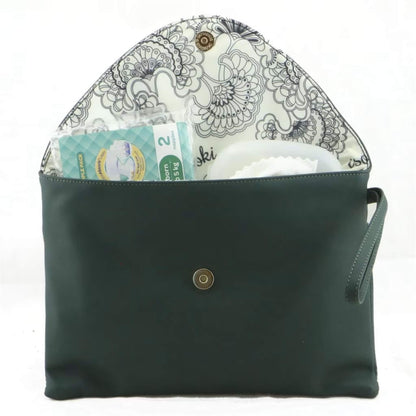 Open green change mat clutch lined with floral patterned fabric, showing nappies, wipes, and baby essentials neatly stored inside.